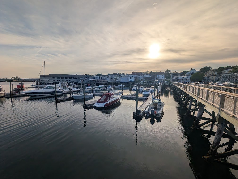 Boothbay Harbor at golden hour — moored boats in the marina and the long footbridge reaching across the water