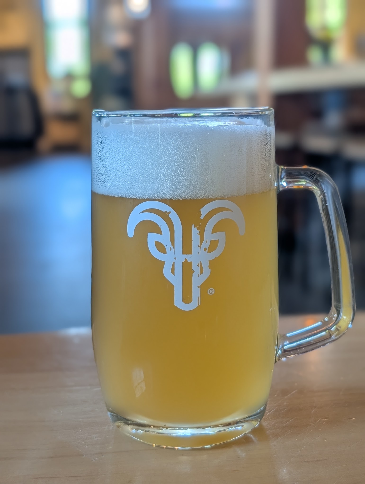 A Helles lager in a glass mug with the von Trapp goat etched on the side — drinking the anniversary lager at the anniversary lodge, mountains out the window