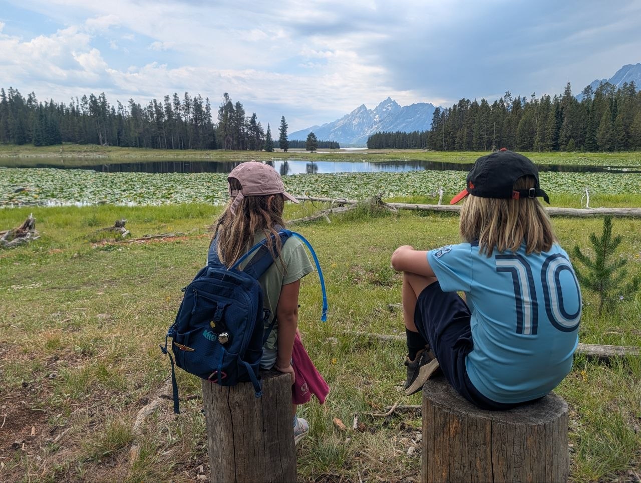 Two kids sitting on posts at the edge of Heron Pond, looking out at the mountains