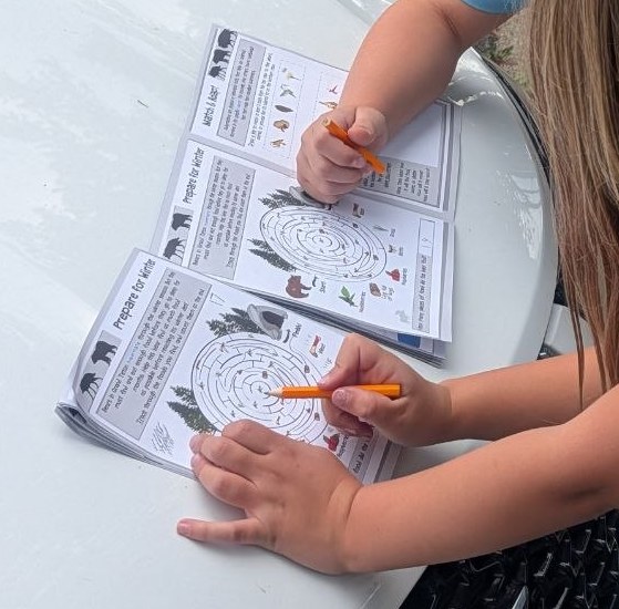Two Junior Ranger booklets open on the hood of the car, pencils in hand